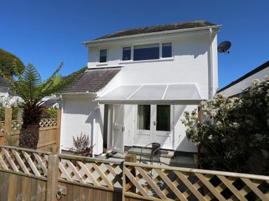 A two-story white house with a small fenced garden patio and a chair at Cuckooland in Borth-Y-Gest