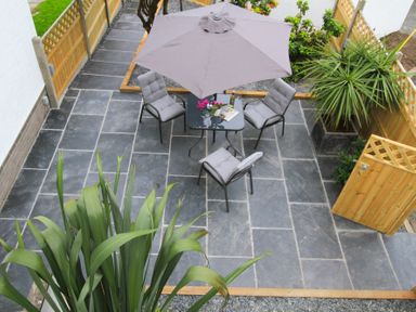 An outdoor patio with a table, four cushioned chairs, a large umbrella, plants, and wooden fencing at Cuckooland in Borth-Y-Gest