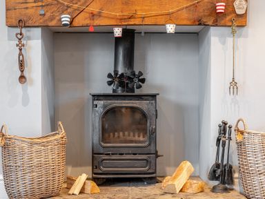 A living room with a wood stove and baskets at Curragho in Trearddur Bay