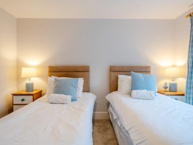 A bedroom with twin beds and lamps at Curragho in Trearddur Bay