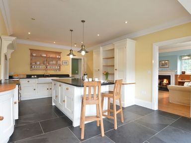 A kitchen with an island and two wooden chairs with a view into a living room with a fireplace at Dinas Noddfa in Nant Gwynant