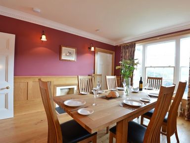A dining room with a wooden table set with plates glasses and a vase of flowers at Dinas Noddfa in Nant Gwynant