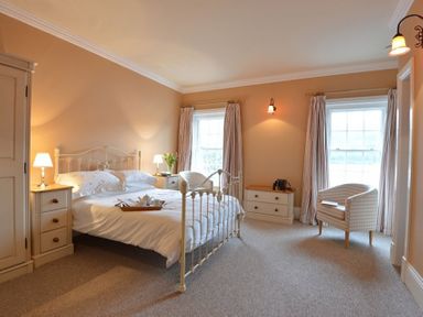 A bedroom with a bed nightstands lamps armchairs and windows at Dinas Noddfa in Nant Gwynant