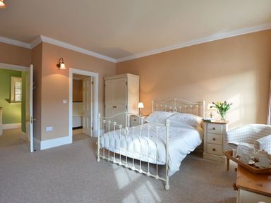 A bedroom with a metal bed frame two bedside tables lamps a wardrobe a checkered armchair and a tray with teacups at Dinas Noddfa in Nant Gwynant