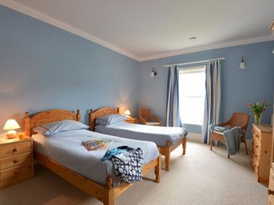 A bedroom with two single beds nightstands lamps wicker chairs and a window with curtains at Dinas Noddfa in Nant Gwynant