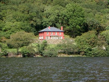 A red house with a slate roof surrounded by trees near a body of water at Dinas Noddfa in Nant Gwynant