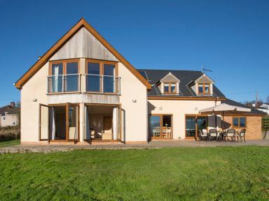 A modern house with large windows and doors opening to a patio with outdoor furniture and umbrella at Dol Fraint in Star