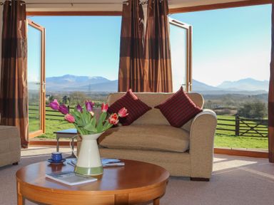 A living room with a wooden table holding a vase of flowers and books two armchairs with cushions and open doors revealing a rural landscape at Dol Fraint in Star