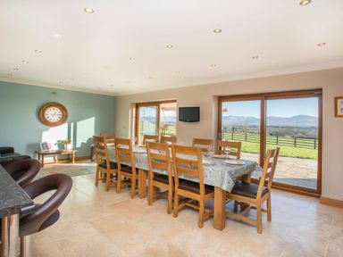 A dining room with a long wooden table covered with a tablecloth and wooden chairs facing glass doors with a view of fields and mountains at Dol Fraint in Star