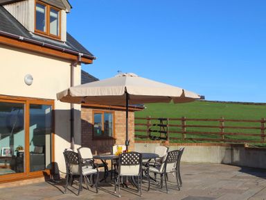 An outdoor patio area with a round table and six cushioned chairs under a large umbrella at Dol Fraint in Star