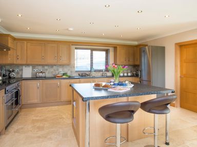 A kitchen with wooden cabinets a central island with stools and flowers on the island at Dol Fraint in Star