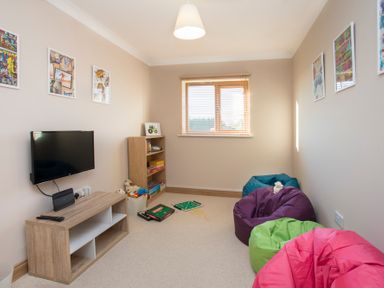 A playroom with a wall-mounted TV bean bags a bookshelf and board games on the floor at Dol Fraint in Star