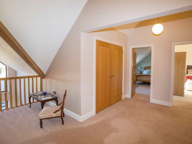 An upstairs hallway with a small table and chair next to a wooden railing and doors leading to bedrooms at Dol Fraint in Star