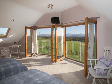 A bedroom with two beds a white chair a small table and open wooden framed glass doors leading to a balcony overlooking green fields at Dol Fraint in Star