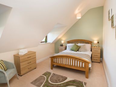A bedroom with a wooden bed frame two bedside tables a chest of drawers a chair and a rug at Dol Fraint in Star