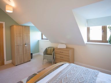A bedroom with a wooden wardrobe a chair with a cushion a wooden dresser with folded towels and a window with blinds at Dol Fraint in Star
