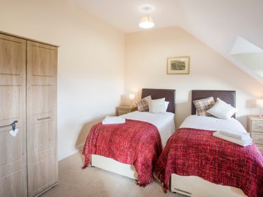 A bedroom with two single beds with red blankets wooden wardrobe and bedside tables with lamps at Dol Fraint Star