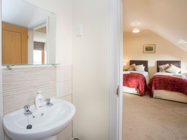 A bathroom sink with mirror and liquid soap next to a bedroom with two single beds with red blankets at Dol Fraint Star