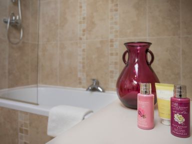 A bathroom with a bathtub tiled in beige with a white towel hanging and bath products with a purple vase on the counter at Dol Fraint in Star