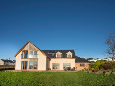 A modern two-story house with large windows and a patio with outdoor furniture at Dol Fraint Star