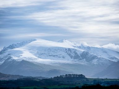 Snow-covered mountains with green hills and trees in the foreground at Dol Fraint in Star