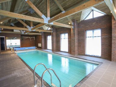An indoor swimming pool with windows and wooden beams at Bryn Eira Tack Room in Llanfair PG
