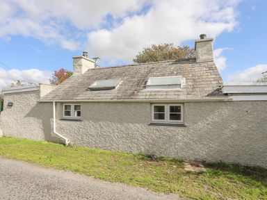 A small cottage with two chimneys two skylights and two windows on a grassy roadside at Ffrwd Cottage in Bodorgan