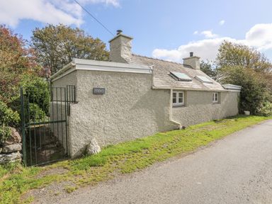 A house with two chimneys and skylights next to a road at Ffrwd Cottage in Bodorgan
