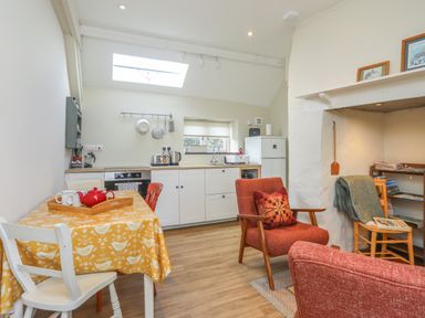 A kitchen and sitting area with a table covered by a yellow cloth and red chairs at Ffrwd Cottage in Bodorgan