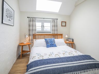 A bedroom with a bed between two wooden bedside tables and a window with curtains at Ffrwd Cottage in Bodorgan