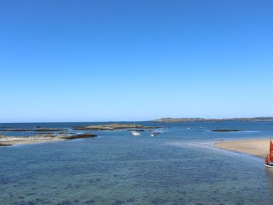A coastal scene with boats on the water and rocky outcrops at Flip Flops in Rhosneigr
