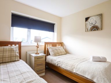 A bedroom with two single beds bedside table with lamp and window at Flip Flops in Rhosneigr