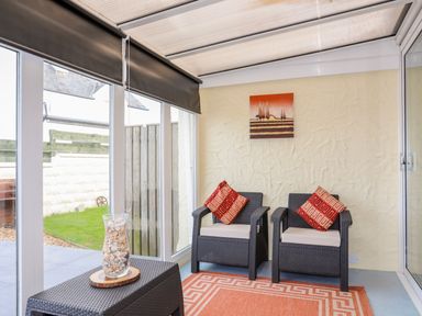 A sunroom with two armchairs with cushions a small table with a vase of shells and a rug at Flip Flops in Rhosneigr