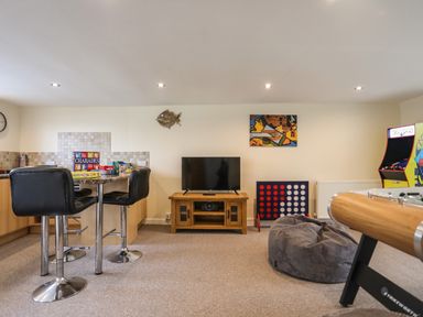 A game room with a television on a wooden stand a bean bag chair a foosball table an arcade machine and a bar table with chairs at Flip Flops in Rhosneigr