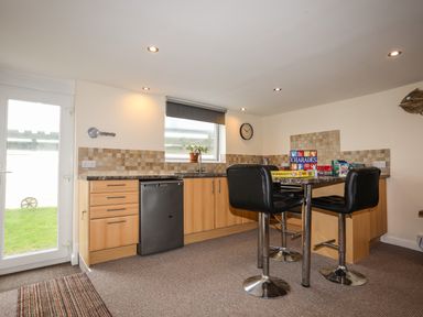 A kitchen with wooden cabinets black dishwasher and a table with black chairs and board games at Flip Flops in Rhosneigr