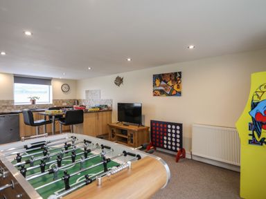 A game room with a foosball table a television on a wooden stand board games on a counter and a large connect four game at Flip Flops in Rhosneigr