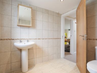 A bathroom with a pedestal sink a wall-mounted mirror and a wooden door open to an adjoining room at Flip Flops in Rhosneigr