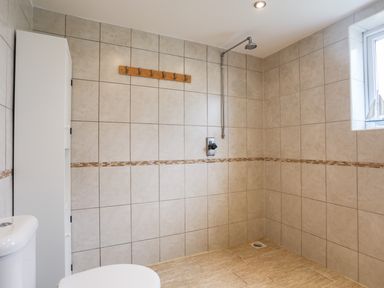 A tiled bathroom with a shower area toilet storage cabinet and window at Flip Flops in Rhosneigr