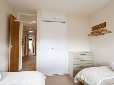 A bedroom with two beds a chest of drawers a closet and wooden hangers on the wall at Flip Flops in Rhosneigr