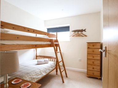 A bedroom with a wooden bunk bed a chest of drawers and a small side table with a lamp at Flip Flops in Rhosneigr
