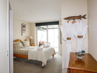 A bedroom with a bed with checked bedding a bedside table with a lamp a dresser with a bowl and two white robes hanging on a fish-shaped hanger at Flip Flops in Rhosneigr