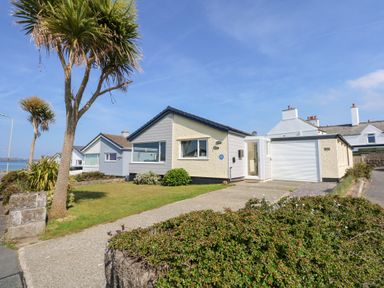 A single-story house with a driveway palm trees and a lawn near the coast at Flip Flops in Rhosneigr