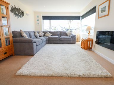 A living room with a grey sectional sofa a white rug wooden cabinet and side tables at Flip Flops in Rhosneigr