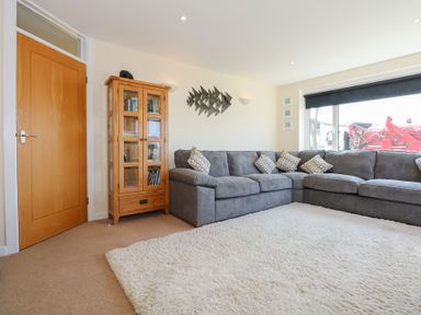 A living room with a grey sectional sofa and a wooden cabinet at Flip Flops in Rhosneigr