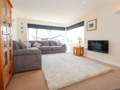 A living room with a gray sofa wooden cabinet white rug and wall-mounted TV at Flip Flops in Rhosneigr
