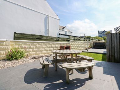 An outdoor patio with a round wooden picnic table and benches a small grass area and surrounding wall at Flip Flops in Rhosneigr