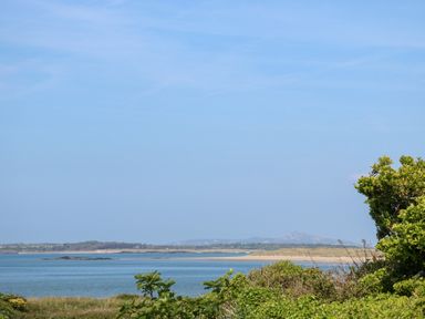 A coastal view with a calm sea grassy foreground and distant hills at Flip Flops in Rhosneigr