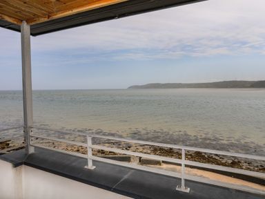 A view of the sea and shoreline from a balcony with a metal railing and roof at Four The Quay in Red Wharf Bay