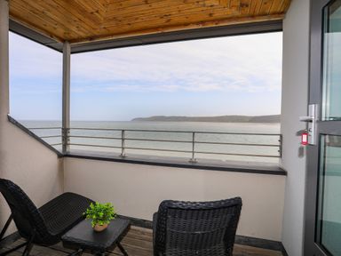 A balcony with two black wicker chairs and a table overlooking the sea at Four The Quay in Red Wharf Bay