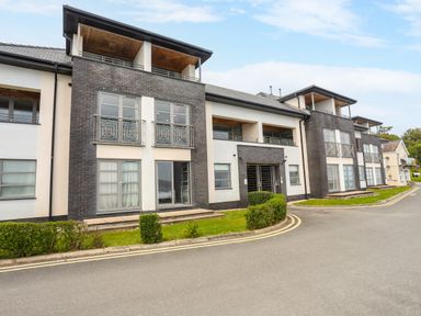 A modern apartment building with balconies and bushes along the road at Four The Quay in Red Wharf Bay